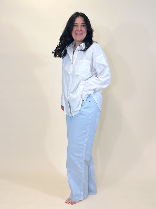 A woman wearing a simply julianne white cotton button-down shirt with a front pocket and light blue denim jeans.